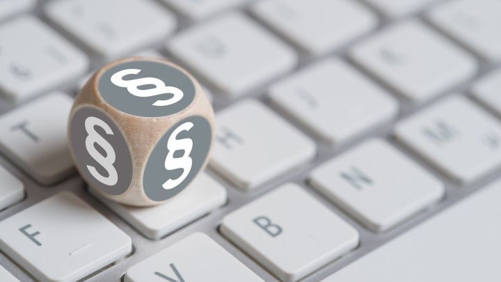 Ein grauer W&uuml;rfel mit Paragraphenzeichen liegt auf einer Computer-Tastatur, was rechtliche Themen im digitalen Kontext symbolisiert.