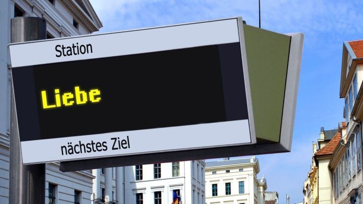 Eine Wegweisung zeigt &bdquo;Liebe&ldquo; als Ziel an; eine attraktive urbane Umgebung unter blauem Himmel umgebt die Station.