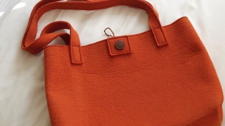 Eine orange Umh&auml;ngetasche aus Filz liegt auf einer hellen Oberfl&auml;che, bereit zum Einsatz f&uuml;r allt&auml;gliche Erledigungen.