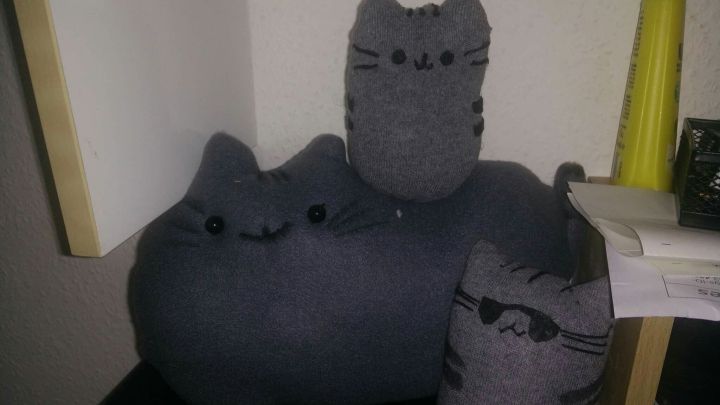 Graue, pl&uuml;schige Katzenkissen stehen gestapelt auf einem Tisch, umgeben von einem gem&uuml;tlichen Raum mit wenig Licht.