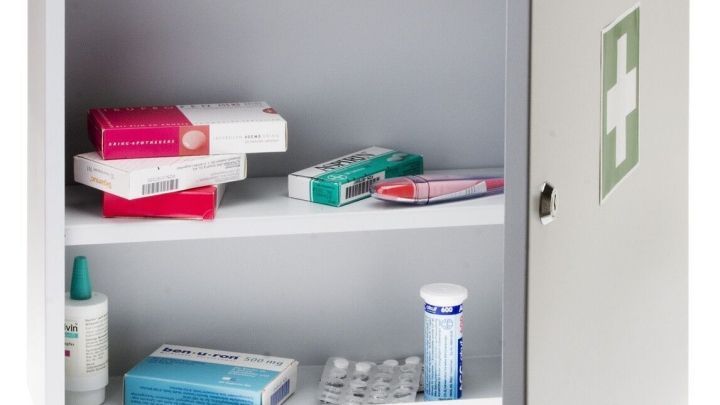 Ein ge&ouml;ffneter Hausapotheke zeigt ordentlich angeordnete Medikamente und Pflegeprodukte in einem neutralen Raum.