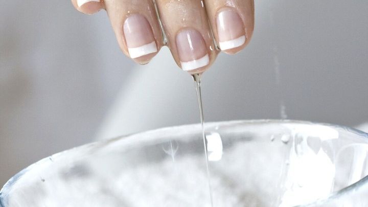 Eine Hand mit gepflegten N&auml;geln dr&uuml;ckt Wasser in eine Sch&uuml;ssel, um raue H&auml;nde zu vermeiden, w&auml;hrend sie in einer hellen Umgebung ist.