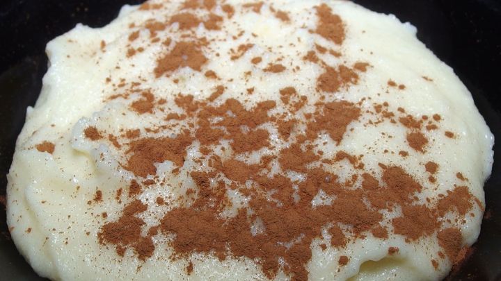 Ein cremiger Grie&szlig;koch liegt in einer dunklen Sch&uuml;ssel, bestreut mit Zimt und zeigt sich als k&ouml;stliches Dessert.