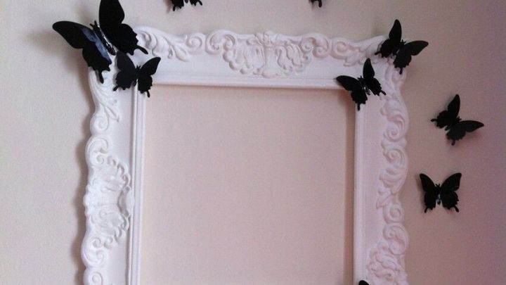 Ein eleganter Bilderrahmen aus Styropor-Zierleisten h&auml;ngt an der Wand, umgeben von schwarzen Schmetterlingen, die ihn dekorativ umgeben.