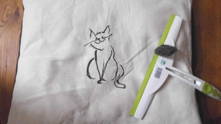 Ein Kissen mit Katzenzeichnung wird mit einem speziellen Werkzeug zur Entfernung von Tierhaaren gereinigt.