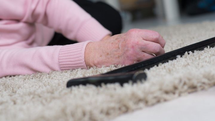 Eine Hand liegt auf einem Teppich, w&auml;hrend ein Gehstock daneben liegt. Die Umgebung wirkt ruhig und h&auml;uslich.