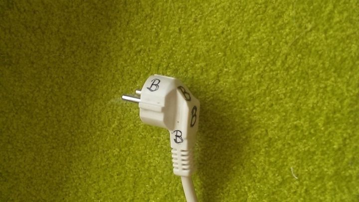 Ein wei&szlig;er Stecker liegt auf einem gr&uuml;nen Teppich und ist nicht mit einem Ger&auml;t verbunden, was Fragen zum B&uuml;geleisen aufwirft.