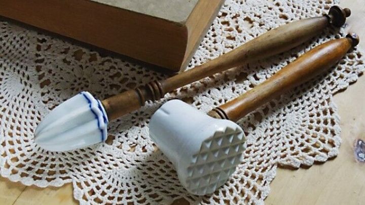 Zwei alte Kochutensilien liegen auf einer Spitzendeckchen, umgeben von einem Holzuntergrund und einer geschlossenen Buch.