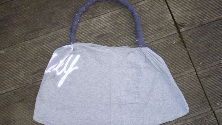 Eine umweltfreundliche Tragetasche aus einem alten T-Shirt liegt auf einem Holzboden, bereit zur Verwendung.