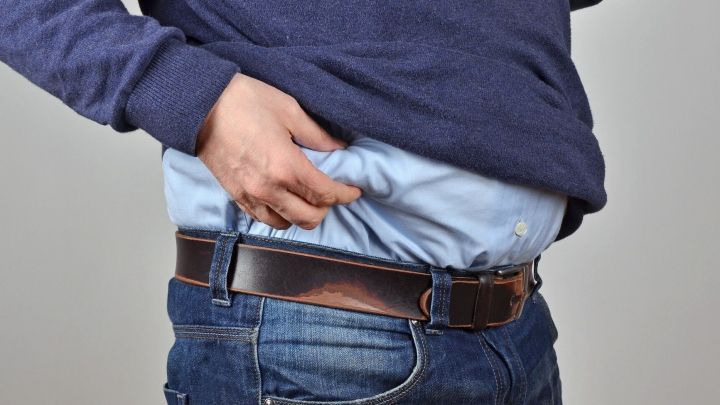 Eine Person greift an ihren Bauch, w&auml;hrend sie eine zu enge Hose tr&auml;gt, was zeigt, wie Abnehmen am Bauch notwendig sein kann.