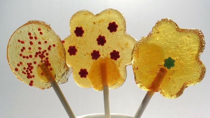 Bunte Lollies stehen in einem hellblauen Becher und erfreuen mit fr&ouml;hlichen, s&uuml;&szlig;en Formen und bunten Streuseln.