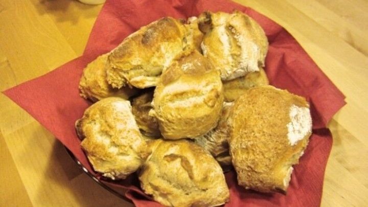 Krosse Br&ouml;tchen liegen auf rotem Papier in einem Korb und laden zum Genie&szlig;en ein, perfekt f&uuml;r ein Fr&uuml;hst&uuml;ck oder Snack.