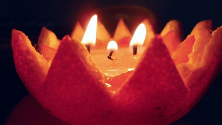 Eine &Ouml;llampe in einer Orangenschale brennt, w&auml;hrend sie in einem dunklen Raum sanft leuchtet und stimmungsvolles Licht verbreitet.