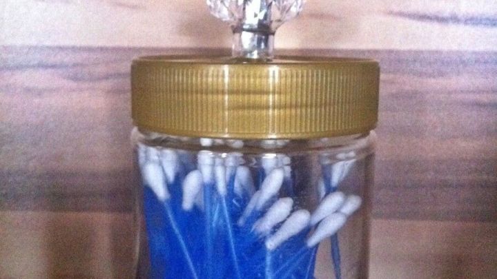 Ein leeres Schraubglas mit goldenem Deckel befindet sich auf einem Tisch und enth&auml;lt zahlreiche wattierte Ohrenst&auml;bchen.