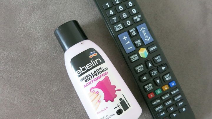 Ein Nagellackentferner steht neben einer Fernbedienung auf einem grauen Untergrund, bereit, Tipp-Ex-Flecken zu entfernen.