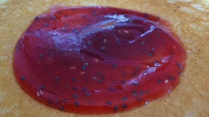 Eine rote Erdbeermarmelade mit sichtbaren Chia-Samen ist auf einem hellen, runden Pfannkuchen plaziert.