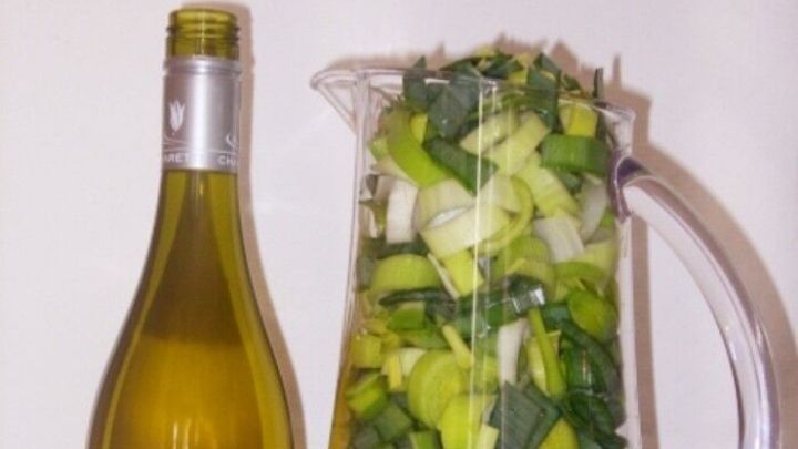 Ein Krug aus Glas ist gef&uuml;llt mit frischem Lauch, daneben steht eine Flasche Wei&szlig;wein auf einer Holzoberfl&auml;che.