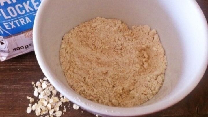 Eine Sch&uuml;ssel mit feinem Hafermehl steht auf einem Tisch, umgeben von Haferflocken und einer Verpackung.