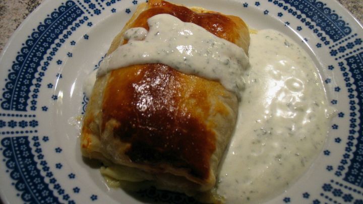 Leckere Spargel-Schinken Taschen auf einem Teller, garniert mit einer cremigen Kr&auml;utersauce neben dem knusprigen Geb&auml;ck.