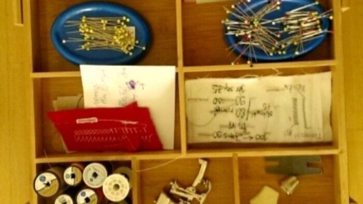 Eine Schublade mit N&auml;hutensilien organisiert, darunter Spulen, Stecknadeln und eine Schere, bereit zum N&auml;hen.