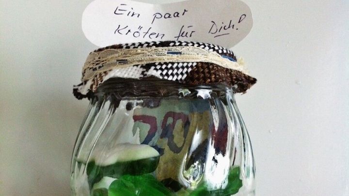 Ein Glas mit gr&uuml;nen und wei&szlig;en S&uuml;&szlig;igkeiten, das als Geldgeschenk dekoriert ist, steht auf einem wei&szlig;en Hintergrund. Auf dem Deckel steht: "Ein paar Kleingeld hier".