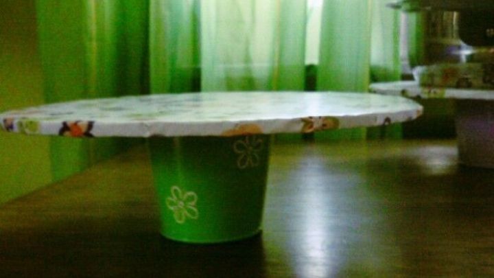 Eine Etagere mit Geheimfach steht auf einem Tisch aus einem gr&uuml;nen Becher, umgeben von gr&uuml;nen Vorh&auml;ngen im Hintergrund.