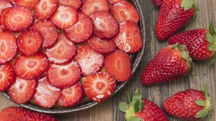 Kreisrunde Obstkuchen mit frischen Erdbeeren, die auf einem Holzbrett sch&ouml;n angerichtet sind, umh&uuml;llt von Gelatine.