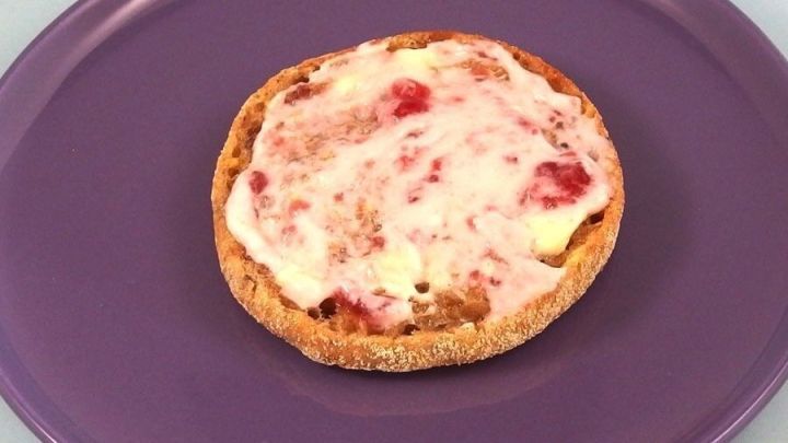 Ein runder Toast mit Quark und Fruchtaufstrich liegt auf einem lila Teller, ideal f&uuml;r ein leckeres Fr&uuml;hst&uuml;ck.