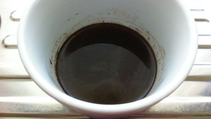 Ein wei&szlig;er Becher mit dunklem Inhalt steht auf einer Metalloberfl&auml;che, bereit f&uuml;r die Anwendung einer effektiven Haarkur.