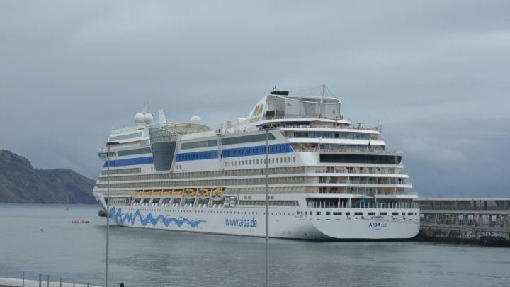 Ein gro&szlig;es Kreuzfahrtschiff liegt ruhig im Hafen, umgeben von grauem Himmel und ruhigem Wasser, bereit f&uuml;r die Reise.