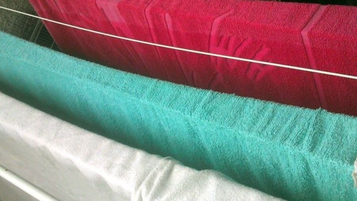 Bunte Handt&uuml;cher h&auml;ngen auf einem W&auml;schest&auml;nder, w&auml;hrend die Sonne scheint und ein Sommerstil f&uuml;r Stromersparnis im Trockner gef&ouml;rdert wird.