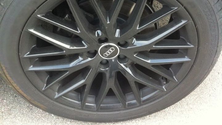 Ein schwarzer Autoreifen mit sportlichem Felgendesign steht auf einer asphaltieren Oberfl&auml;che und wartet auf die n&auml;chste Fahrt.