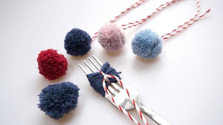 Mini PomPoms aus Wolle liegen auf einem Tisch, w&auml;hrend eine Gabel benutzt wird, um sie zu formen und zu binden.