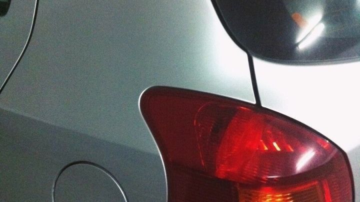 Ein silbernes Auto steht in einer Garage. Der Heckbereich wird gereinigt und gepflegt, sichtbar unter k&uuml;nstlichem Licht.