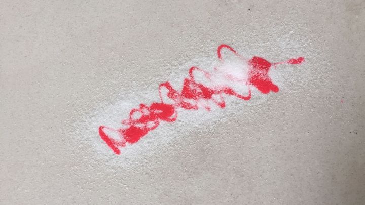 Ein roter Nagellackfleck liegt auf einer Feinsteinfliese, sichtbar und in einem sauberen Raum.