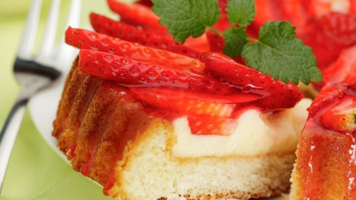 Ein St&uuml;ck Torte mit frischen Erdbeeren liegt auf einem Teller, umgeben von einer gr&uuml;nen Tischdecke.