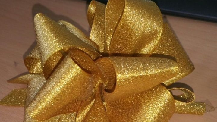 Eine gl&auml;nzende goldene Pompon Schleife liegt auf einem Holzschreibtisch, bereit f&uuml;r Geschenke oder Dekorationen.