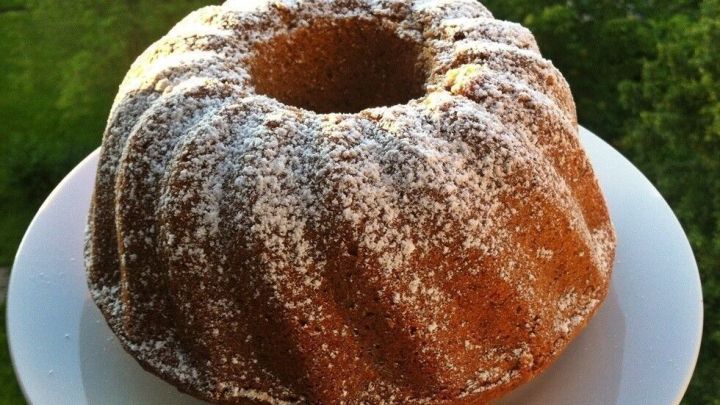 Ein Nuss-Gugelhupf steht auf einem wei&szlig;en Teller, best&auml;ubt mit Puderzucker, vor einem gr&uuml;nen Hintergrund.