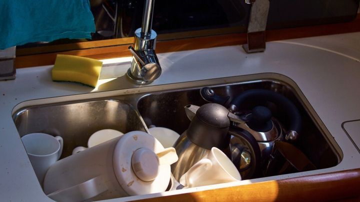 Im Sp&uuml;lbecken stehen verschmutzte Thermoskannen und Thermobecher, w&auml;hrend Licht von oben auf das Geschirr f&auml;llt.