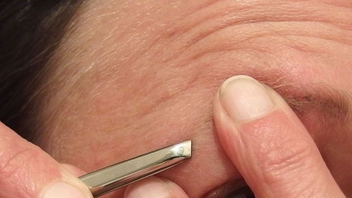 Eine Hand zupft sanft an einer Augenbraue, w&auml;hrend die Umgebung weich und neutral gehalten ist, um die Technik zu verdeutlichen.