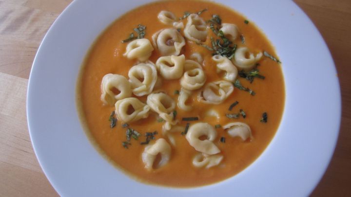 Eine cremige Karottensuppe liegt in einer wei&szlig;en Sch&uuml;ssel, die mit kleinen Teigtaschen und Kr&auml;utern garniert ist.