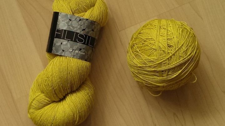 Ein gelber Wollstrang liegt neben einem gleichfarbigen Kn&auml;uel auf einem hellen Holztisch und wartet auf die n&auml;chste kreative Nutzung.