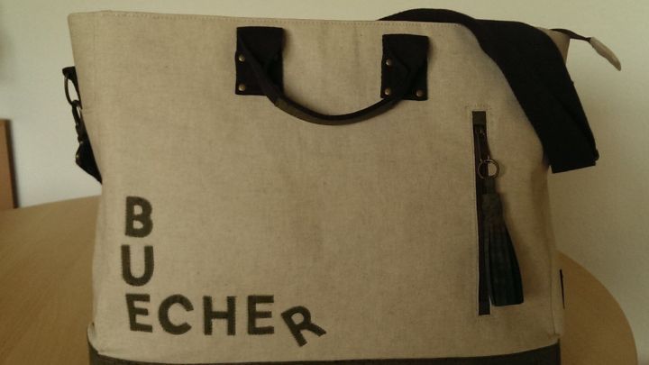 Eine stylische Tasche aus Korkstoff liegt auf einem Tisch und pr&auml;sentiert die Aufschrift "BUECHER" in gro&szlig;en Buchstaben.