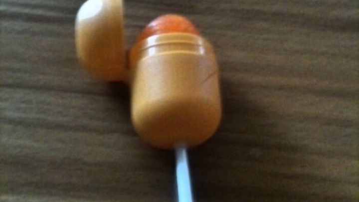 Ein Lolli steckt in einer orangefarbenen Aufbewahrungsbox, die offen auf einem Holzuntergrund liegt.