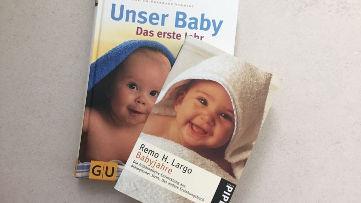 Zwei Baby-Ratgeber liegen auf einem hellen Tisch, einer zeigt ein Baby im Handtuch, der andere hat ein grinsendes Baby.
