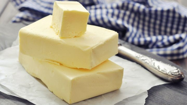 Drei St&uuml;cke Butter liegen auf einem wei&szlig;en Papier neben einem L&ouml;ffel, im Hintergrund ist ein kariertes Tuch sichtbar.