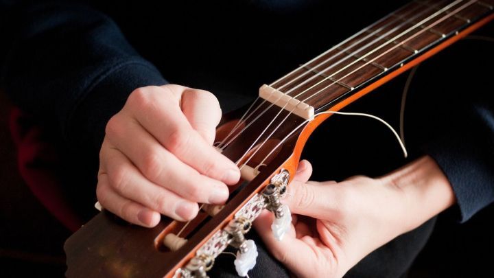 Eine Hand repariert eine alte Gitarre, indem sie die Saiten anpasst, um sie wieder bespielbar zu machen.