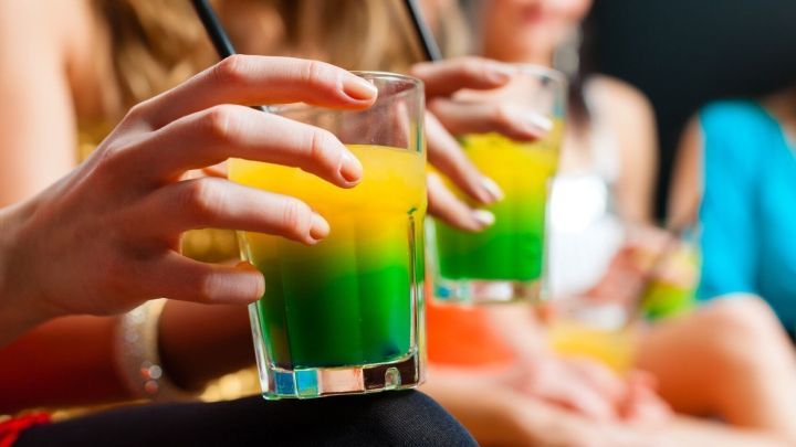 Bunte Cocktails werden in Gl&auml;sern gehalten, w&auml;hrend eine Gruppe von Freunden entspannt zusammen sitzt.