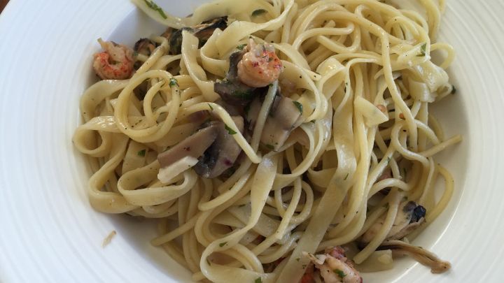 Bandnudeln liegen auf einem wei&szlig;en Teller, umgeben von Miesmuscheln und Pilzen in einer cremigen Sauce.