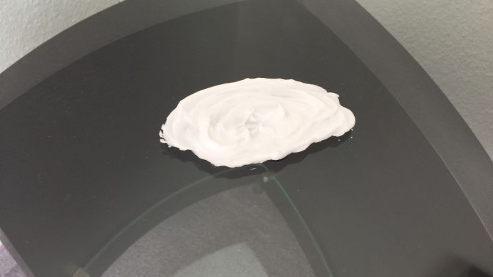 Ein wei&szlig;es, pastenartiges Mittel liegt auf einer glatten Glasoberfl&auml;che, um Nikotin von der Fl&auml;che zu entfernen.